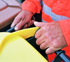 Die Hände des Müllwerkers am Griff einer Gelben Tonne